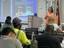 Instructor with powerpoint slide with pesticide safety language on a label with classmates in foreground.