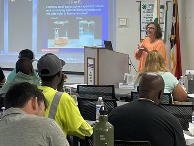 Instructor with powerpoint slide with pesticide safety language on a label with classmates in foreground.