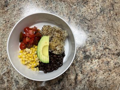 White bowl of quinoa, chopped cherry tomatoes, yellow sweet corn, black beans, and a slice of avocado.
