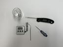 Several food thermometers and metal probes arranged on white surface, dial thermometer in glass
