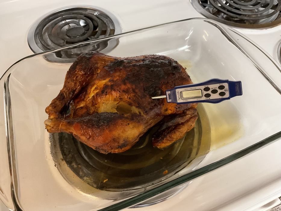 Cooked chicken on a stove top with a thermistor thermometer inserted in it. 