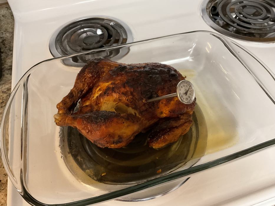 Cooked chicken in a glass dish with a bi-metal thermometer inserted in it.