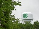 White water tower with green 4-H four-leaf clover logo rising above trees