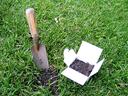 Soil sample box filled with soil sitting on a grass lawn beside a garden trowel.