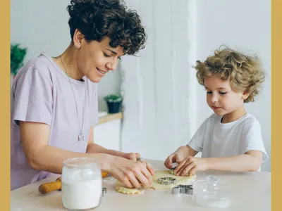 An adult and child baking cookies together at a table, using cookie cutters on the dough.