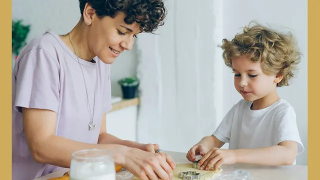 An adult and child baking cookies together at a table, using cookie cutters on the dough.