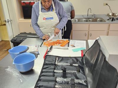 An adult stands behind an open knife carrier bag cutting carrots.