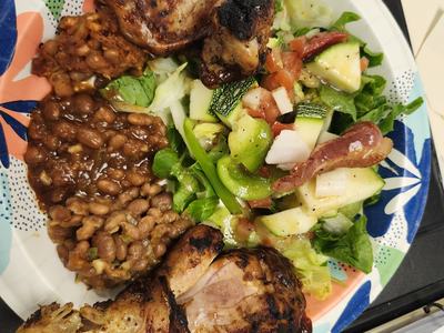 A plate of food containing grilled chicken, fresh summer salad, and baked beans.