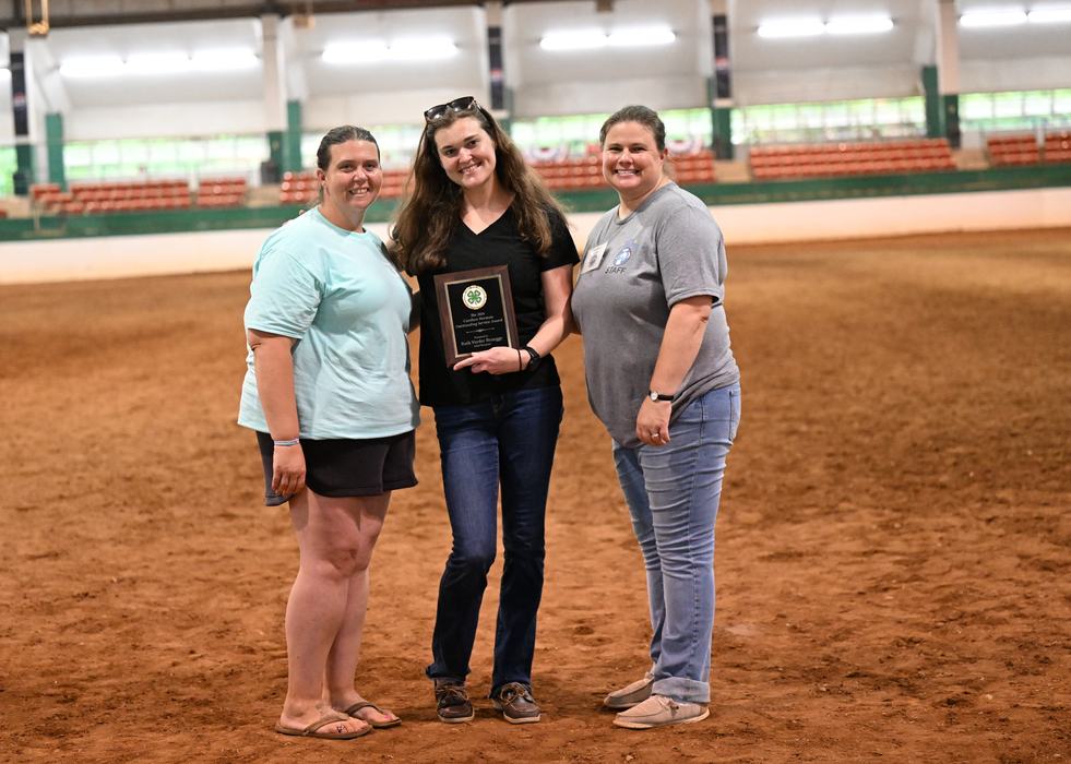 Ruth Vorder Bruegge is holding her plaque for receiving the 2026 Candace Norman Adult Volunteer Leader award. On each side of her are Jessica McVey and Morgan Maness, members of the North Central District 4-H Horse Advisory Council who sponsored the award