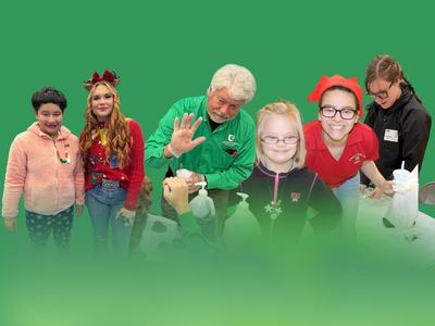 A group of children and adults participating in a holiday-themed 4-H activity, gathered around a table with hands-on materials.