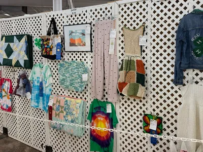 4-H sewing and needlecraft entries displayed on white lattice panels at the 2026 N.C. State Fair, featuring handmade quilts, clothing, knitted and crocheted items, and decorated textiles. Several entries have award ribbons attached.
