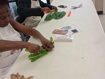 Adults sit at a table learning how to properly cut greens using a chef's knife.