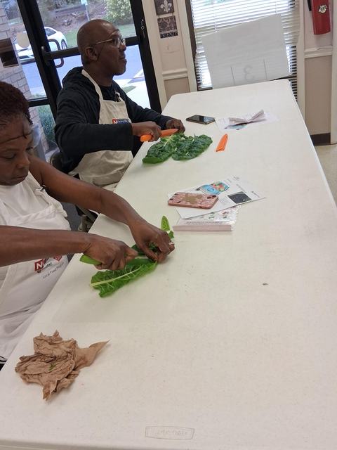 Adults sit at a table learning how to properly cut greens using a chef's knife.