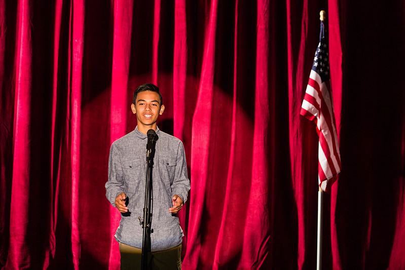 teen speaking in front of red curtains in microphone