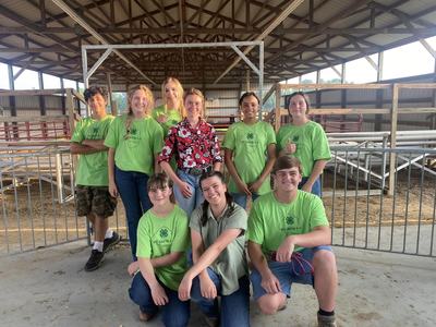 Group of youth in green Pitt County 4-H shirts posing inside a barn.