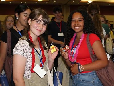 Two smiling girls at a 4-H event wearing leis and holding small plush toys
