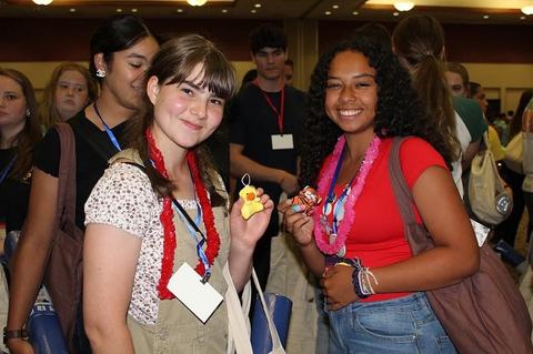 Two smiling girls at a 4-H event wearing leis and holding small plush toys