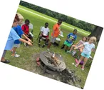 Halifax County 4-H youth and adult leaders gathered outdoors around a fire pit, participating in a hands-on outdoor learning activity.