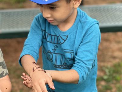 little boy in a blue hat and blue shirt with a worm on his arm