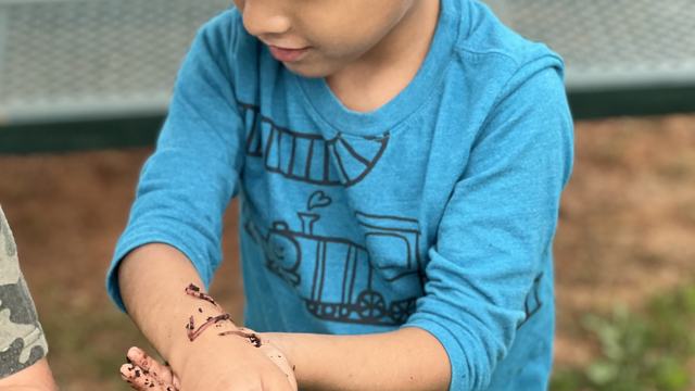 little boy in a blue hat and blue shirt with a worm on his arm