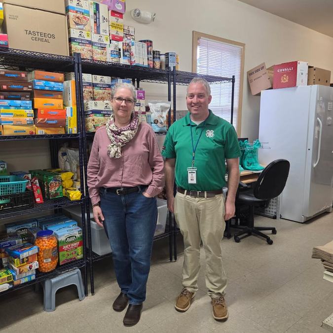 Jonathon Smith and a food pantry partner stand in front of shelves at the pantry