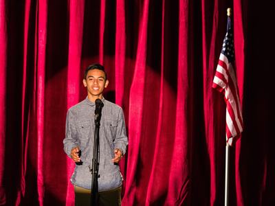 youth speaking at a microphone in front of red curtain