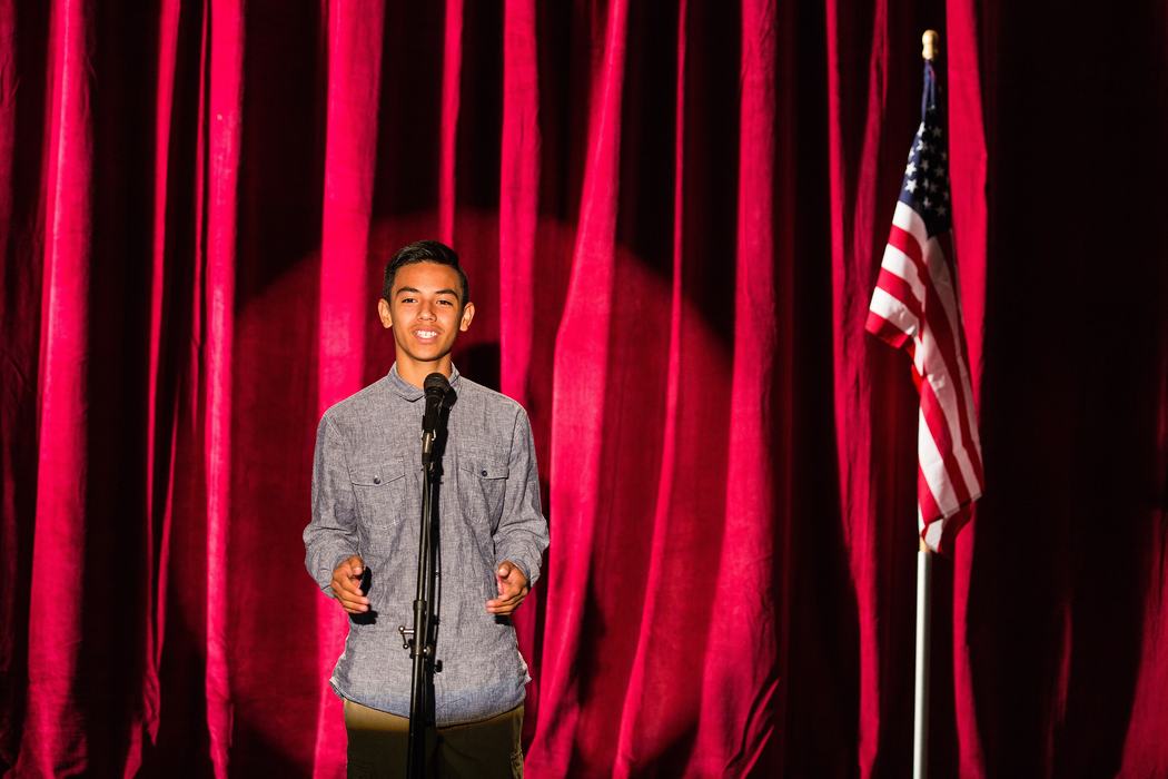 youth speaking at a microphone in front of red curtain