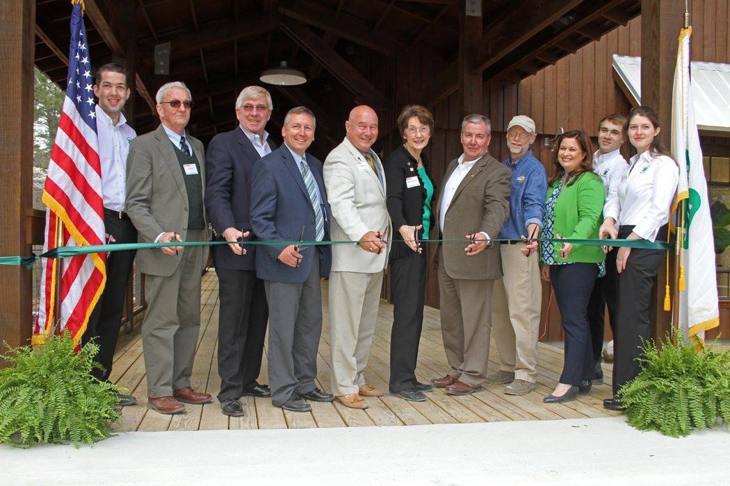 Group of individuals cutting a ribbon during a ceremony at the NC 4-H History and Learning Center at Millstone 4-H Camp.