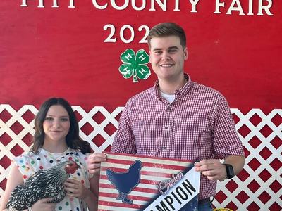 A young woman and a man hold a "Grand Champion Chicken" banner at the fair