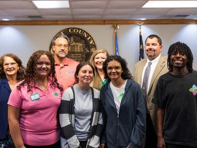 Group of 4-H youth and adults posing together in front of a Pitt County seal.