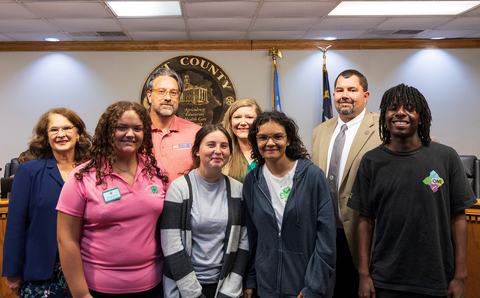 Group of 4-H youth and adults posing together in front of a Pitt County seal.