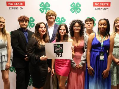 Group of well-dressed youth posing with a Pitt County 2025 NC 4-H Congress sign.