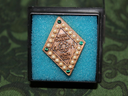 Gold-toned diamond-shaped North Carolina 4-H Honor Club pin set with pearls and green gems, displayed on blue foam in a black box atop green patterned fabric.
