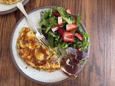 A Spanish tortilla, side salad topped with strawberries, and a little jamon.