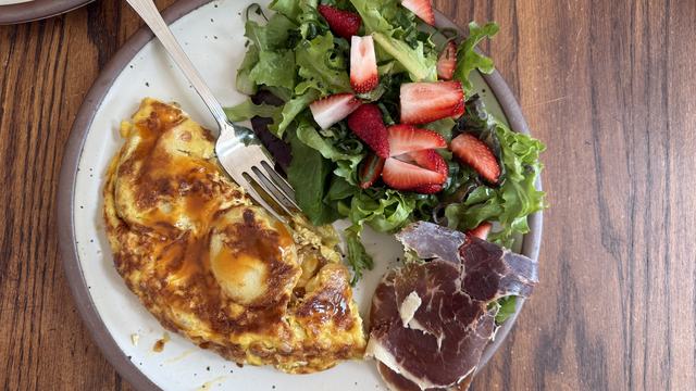 A Spanish tortilla, side salad topped with strawberries, and a little jamon.
