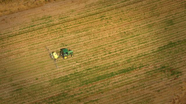 Image of a tractor in a field pulling a sprayer and using it.