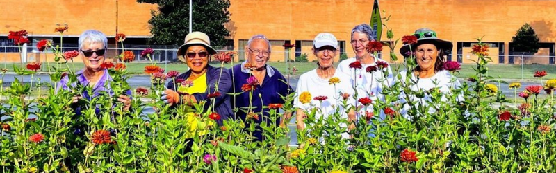 A group of smiling men and women stand among colorful flowers.