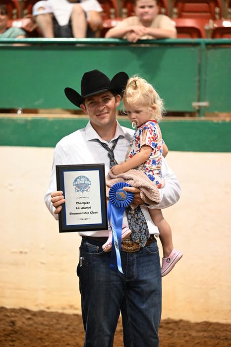 Greyson Marshall is holding his daughter as he accepts his first-place ribbon and plaque for winning the Alumni Showmanship Class.