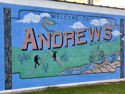 A photograph of a mural with a montage depicting cycling, fishing and hiking.  Includes headline "Welcome to Andrews."