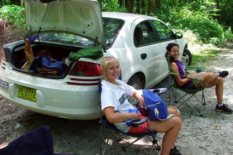 Two people sitting in camp chairs beside car