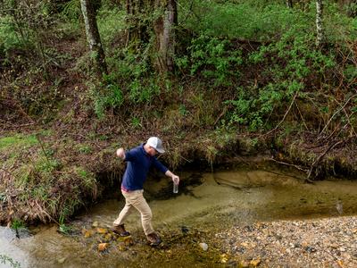 Person crossing creek with insect sample jar