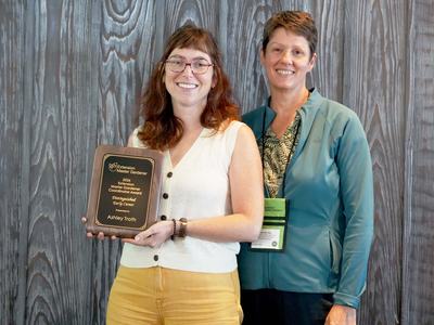 Durham County Horticulture Agent Ashley Troth stands with statewide EMG program manager Charlotte Glen while holding the 2026 Distinguished Early Career Award