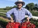 Austin Wrenn, president of the North American Strawberry Association, smiles while holding multiple red baskets of freshly picked strawberries in a farm field.