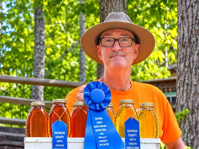local beekeeper with awards and beehive with mountains in the background