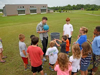 Kids surrounding their instructor waiting to play kickball.