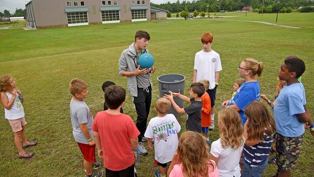Kids surrounding their instructor waiting to play kickball.