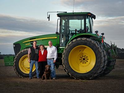 Family at their farm standing in front of a tractor in field