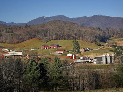 Scenic view of a mountain farm with red barns and silos nestled in rolling hills.