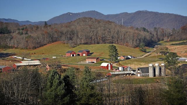 Scenic view of a mountain farm with red barns and silos nestled in rolling hills.