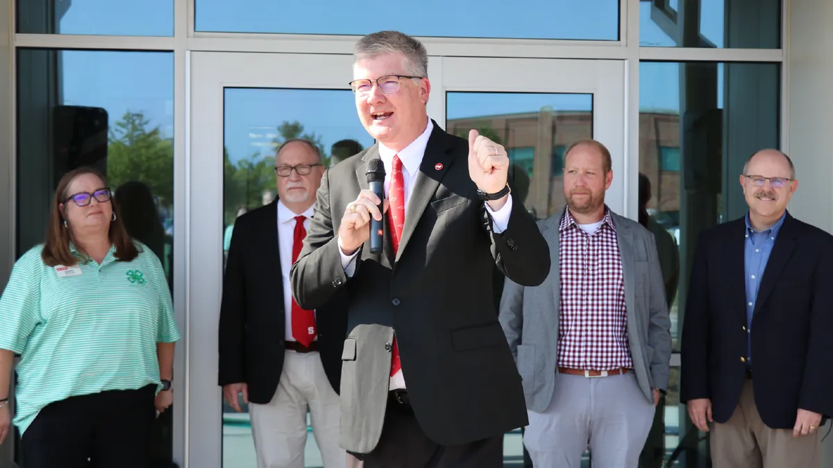 CALS Dean Garey Fox speaks into a microphone outside the CALS Extension Building as 4-H, Extension, agricultural education and departmental leaders stand behind him.
